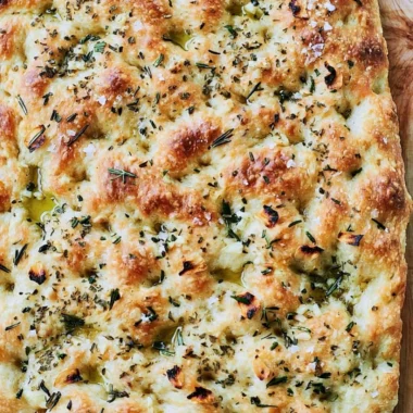 Delicious garlic rosemary focaccia bread garnished with fresh herbs.