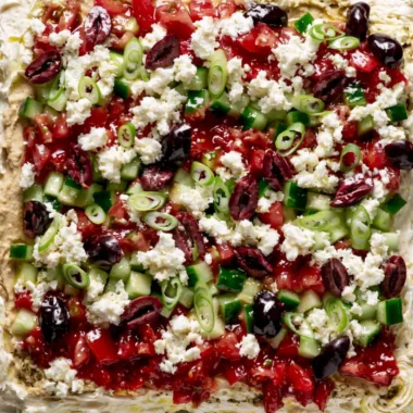 Greek-inspired layered dip with Mediterranean ingredients served in a dish