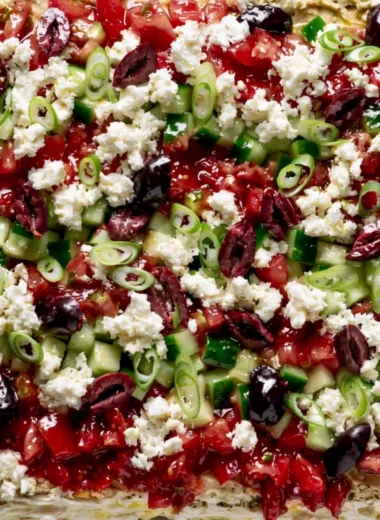 Greek-inspired layered dip with Mediterranean ingredients served in a dish