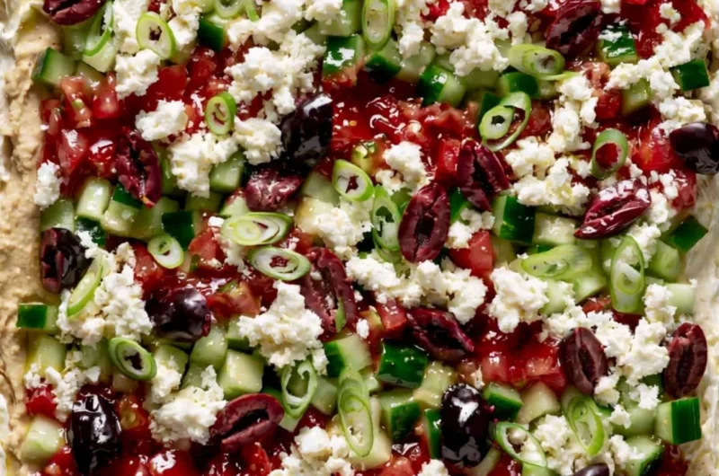 Greek-inspired layered dip with Mediterranean ingredients served in a dish