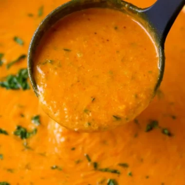 A bowl of homemade tomato basil soup garnished with fresh basil leaves.