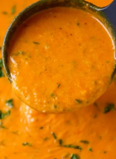 A bowl of homemade tomato basil soup garnished with fresh basil leaves.