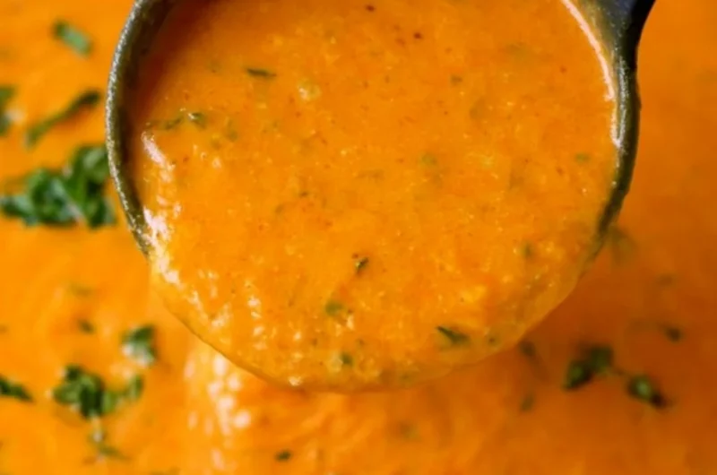 A bowl of homemade tomato basil soup garnished with fresh basil leaves.